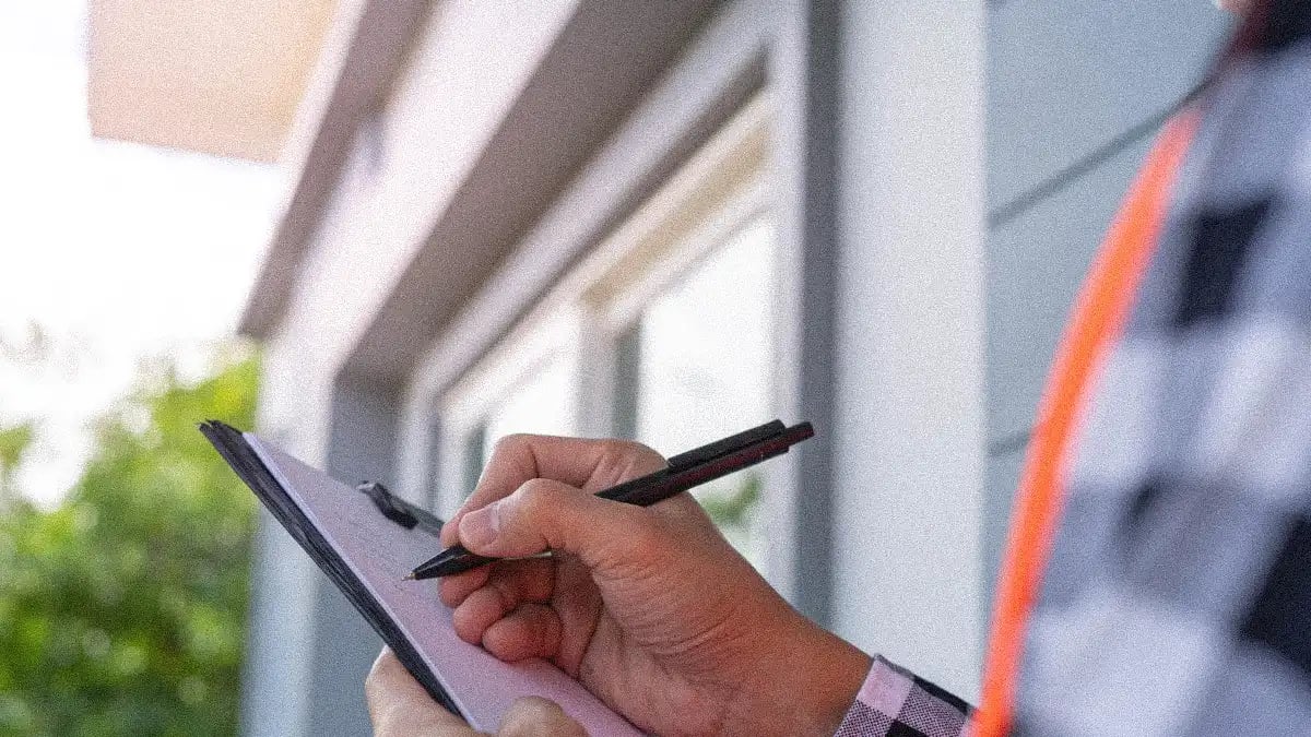 A restorer holding a clipboard and pen, writing or taking notes of a water damage SOP in an outdoor setting with a building in the background.