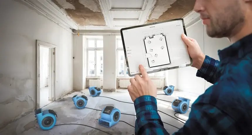 Restoration contractor in water damage job site with seven blue air movers documenting the placement of each equipment using the magicplan app with a sketch on an ipad.