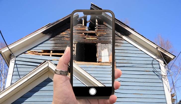Claims adjuster assessing and documenting a structural lightning damage oh a house roof by taking pictures with his smartphone