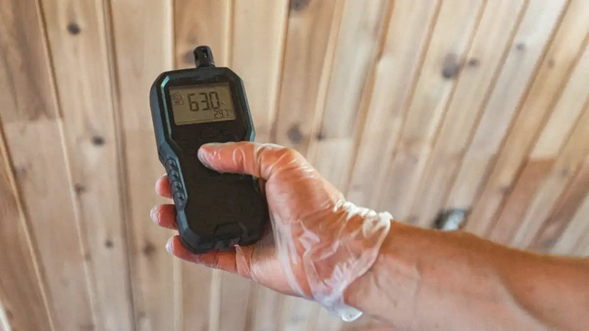 Restoration contractor holding a black moisture meter to map moisture on hardwood using a plastic glove 